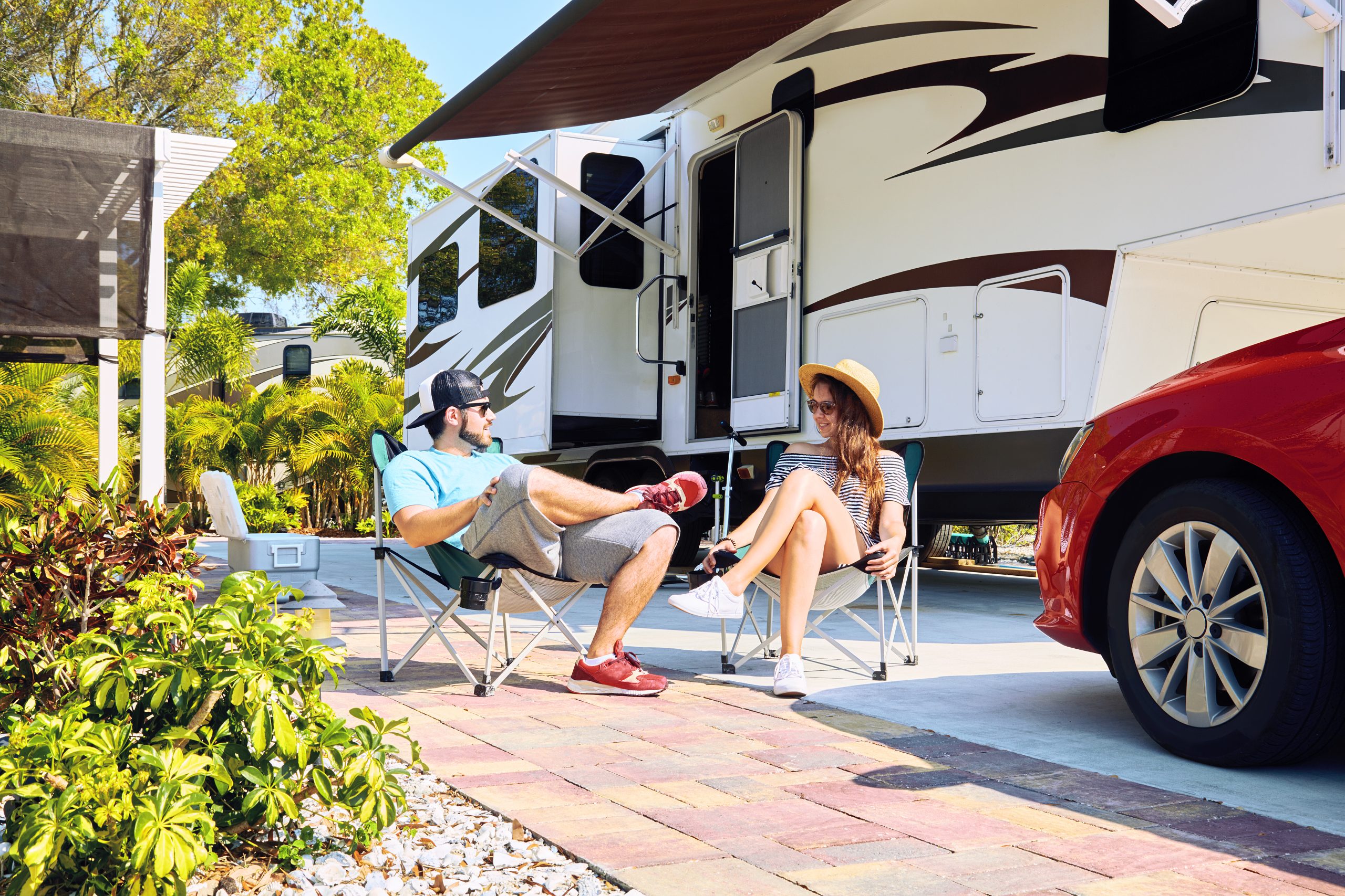 Young couple sits on chairs near camping trailer and car